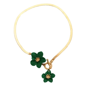 Detailed shot of golden flat snake chain necklace with green flower pendants and toggle clasp