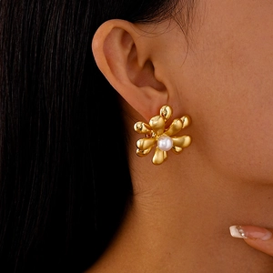 Détail de la boucle d'oreille fleur dorée avec perle blanche sur l'oreille
