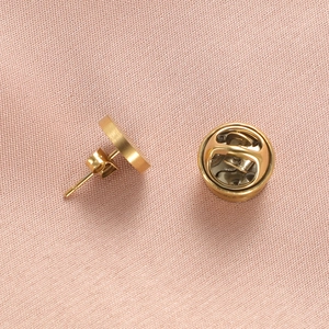 Polished golden stainless steel pin back and butterfly clasp on pink fabric background