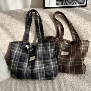 Detail of plaid tote bags in black-grey and red-brown wool fabric on a soft beige sofa