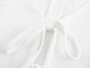 Detail of white sleeveless dress showing tie-up bow and ruffle trim fabric texture
