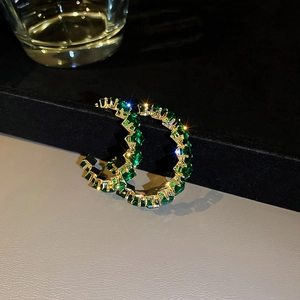 Macro shot of C-shaped gold earrings with sparkling green zircon stones on a dark background