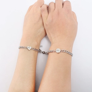 Detail of couple bracelets with magnetic heart and round charms on Cuban chains