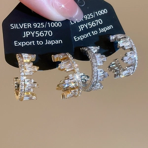 Macro detail of gold and silver C-shaped 925 silver earrings with baguette-cut zircon stones