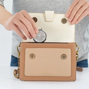 Close-up of a portable rhinestone-studded round pill box placed into a brown leather handbag