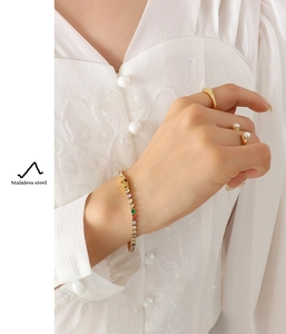 Detail of colorful zircon tennis bracelet and gold rings on model in lace shirt