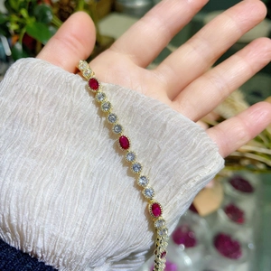 Elegant gold bracelet with red oval ruby-style stone and white zircons on white sleeve