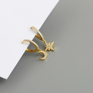Detail of asymmetric gold hoop earrings with star and moon charms and zircons