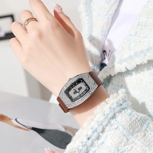 Detail of tonneau diamond watch with brown silicone strap worn on female wrist