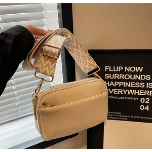 Detail of cream crossbody bag featuring woven geometric strap and gold-tone hardware zipper