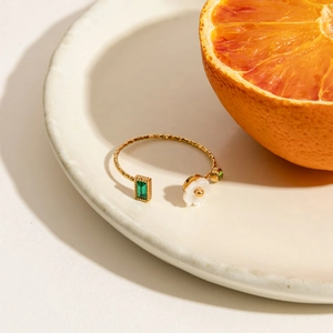 Detail of adjustable gold ring with green gems and flower on a ceramic plate