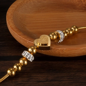 Macro view of gold beaded bracelet with a frosted heart charm and sparkling pavé rings
