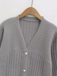Detailed view of grey knit cardigan featuring elegant pearl buttons and deep V-neck design