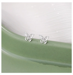 Macro shot of silver butterfly stud earrings on a mint ceramic edge with soft fabric