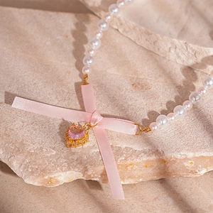 Elegant pearl necklace with pink silk bow and heart-shaped gemstone on stone surface