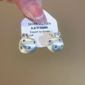Detail of silver apple stud earrings with brushed finish and star-shaped zircon inlays