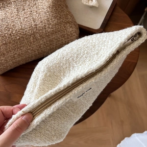 Close-up of a textured beige tweed makeup bag with silver zipper and woven side label