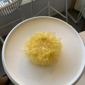 Detail of vibrant yellow pleated organza hair scrunchie on a white ceramic plate