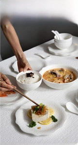 Detail of embossed white ceramic tableware set with scalloped edges and floral texture
