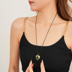 Close-up of a vintage heart pendant with green gemstone on a black cord necklace