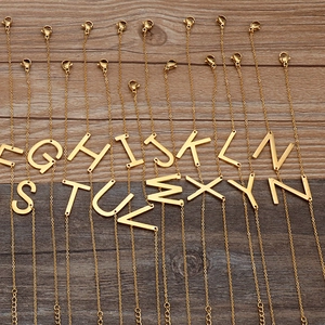 Minimalist gold-plated stainless steel initial pendant necklaces on dark wood background