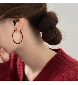 Close-up of red twisted hoop earrings worn by a model in a red knit sweater