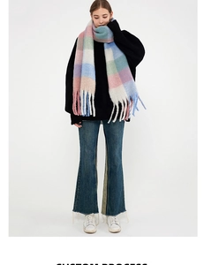 Full-body model view of a thick multicolored plaid scarf with long fringe and tassels