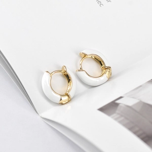 Minimalist white enamel and gold-plated geometric round hoop earrings on a book
