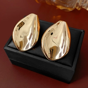 Macro detail of glossy gold leaf-shaped earrings on a black display surface