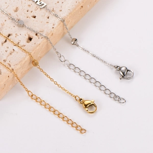 Gold and silver ankle bracelets with Love pendant on beige stone display