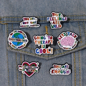 Set of 7 inspirational mental health enamel pins on a blue denim jacket pocket