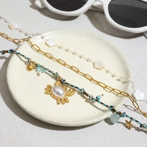 Tre bracciali dorati a strati con perle, intreccio blu e ciondoli a granchio su piatto