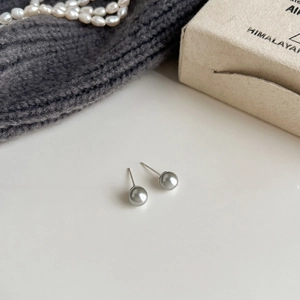 Detailed view of silver grey pearl earrings with s925 needles on textured background