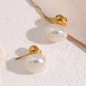 Macro view of 18K gold plated pearl stud earrings on a surface with water droplets