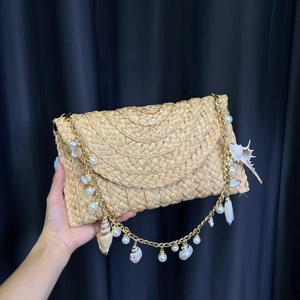 Detail of hand-woven straw envelope bag featuring decorative pearl and seashell charms