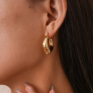 Close-up of elegant gold twisted hoop earring worn on a model with polished mirror finish
