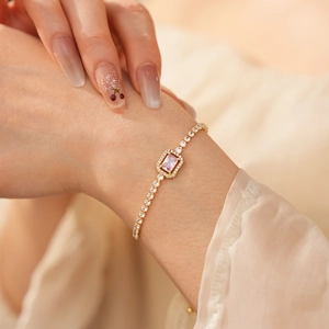 Detail of adjustable gold tennis bracelet with a rectangular pink zircon and halo