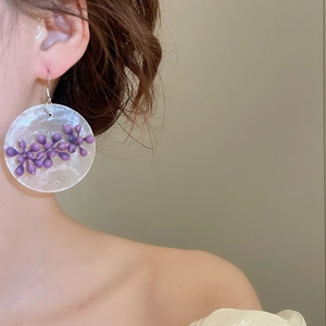 Detailed view of large round pearl-textured earrings with purple floral tassels