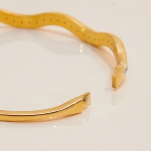 Dettaglio del bracciale rigido in acciaio inossidabile dorato 18K con design a onde e chiusura