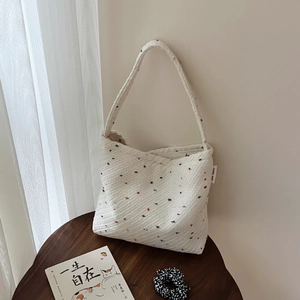 Dettaglio di una borsa tote in maglia bianca con puntini colorati su uno sgabello di legno