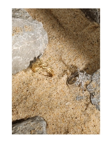 Artistic gold and silver rings with fluid texture displayed on natural sand and stones