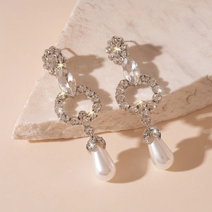 Macro detail of silver floral teardrop earrings with crystals and faux pearls on marble
