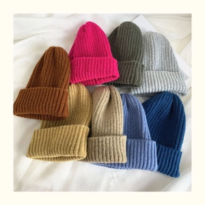 Flat lay of colorful rib-knit beanies in various shades on white wrinkled fabric background