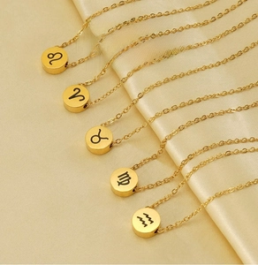 Dettaglio delle collane zodiacali dorate con simboli incisi su sfondo di raso champagne