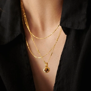 Layered gold necklace featuring a round brown gemstone pendant worn on a model