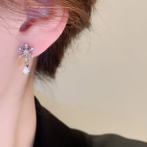 Close-up of sparkling snowflake earrings with teardrop zircon drop on model ear