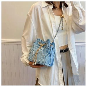 Detail of blue denim bucket bag featuring frayed edges, diamond quilt, and pearl tassels