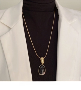 Close-up of a vintage resin oval pendant necklace on a gold snake chain and black sweater