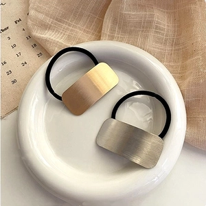 Black high-elastic hair ties with gold and silver rectangular metal buckles on a white tray