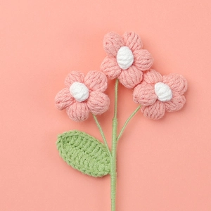 Detailed close-up of handmade crochet puff flowers in pink yarn with green leaves